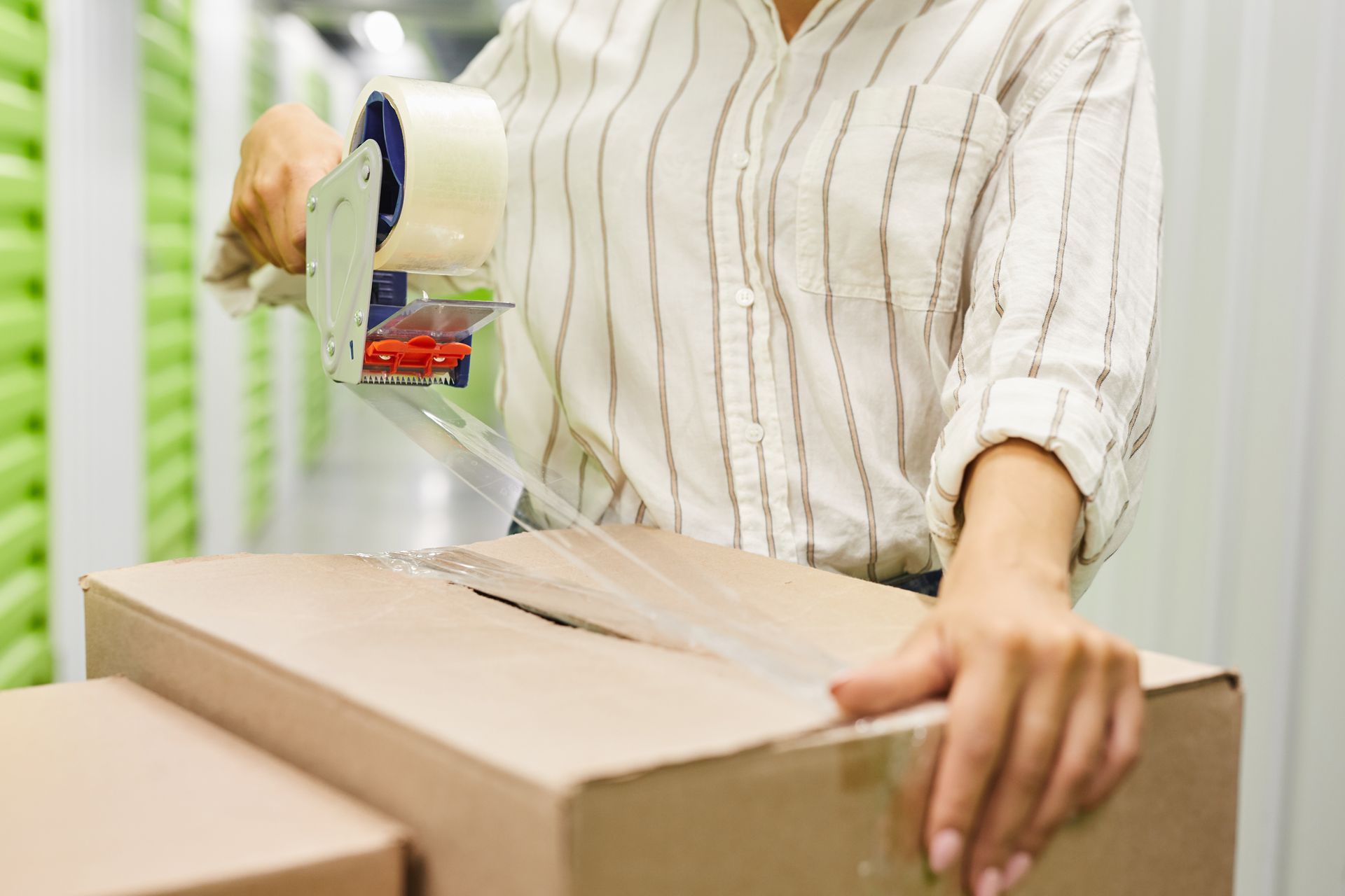 Person sealing a cardboard box with tape in a storage unit.