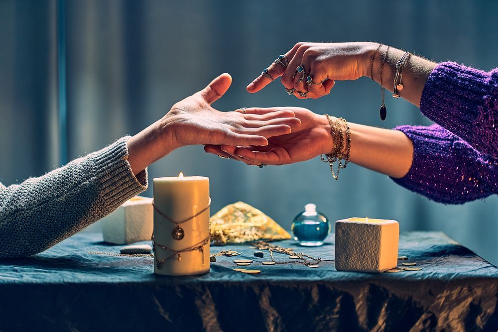 Hands of a fortune teller examining the palm of a person at a table with candles and crystals.
