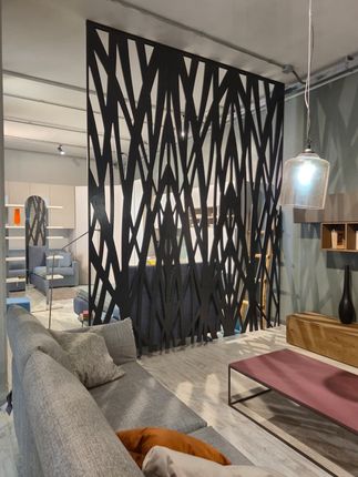 Un separé geometrico nero separa lo spazio abitativo con divano grigio, elementi in legno e illuminazione moderna.