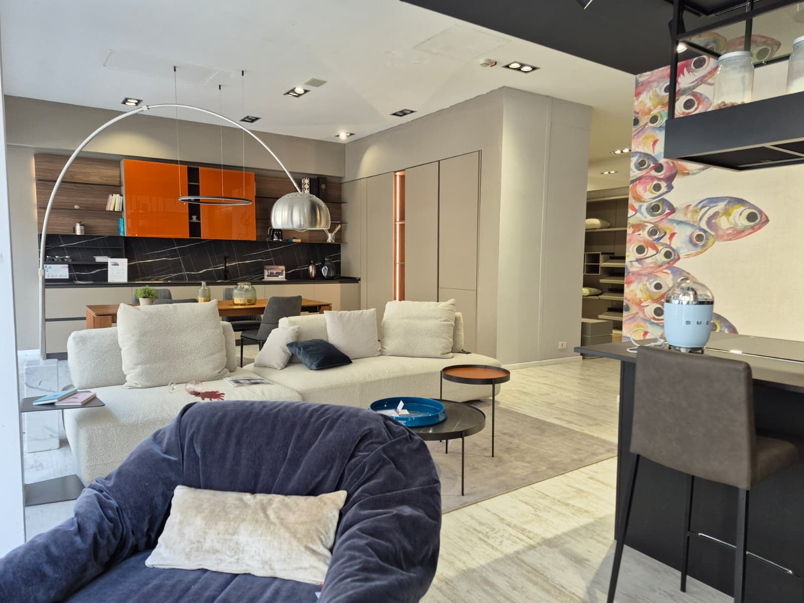 Soggiorno moderno con divano beige, poltrona blu, mobili arancioni e quadri colorati alle pareti.