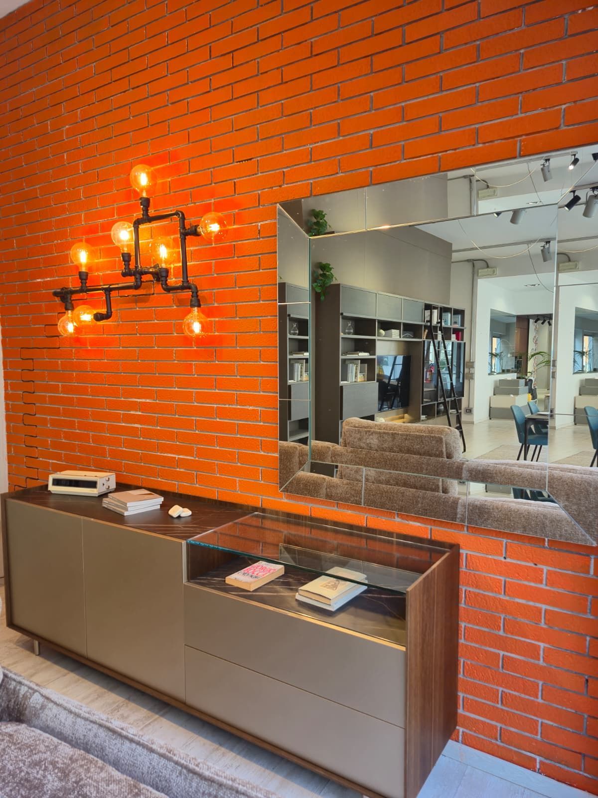 Parete in mattoni arancioni con una moderna consolle, uno specchio e un lampadario artistico.