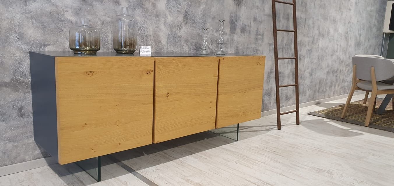 Credenza in legno con gambe in vetro, piano grigio e ante coordinate. Due vasi sul piano superiore. Scala e sedia marroni sullo sfondo.