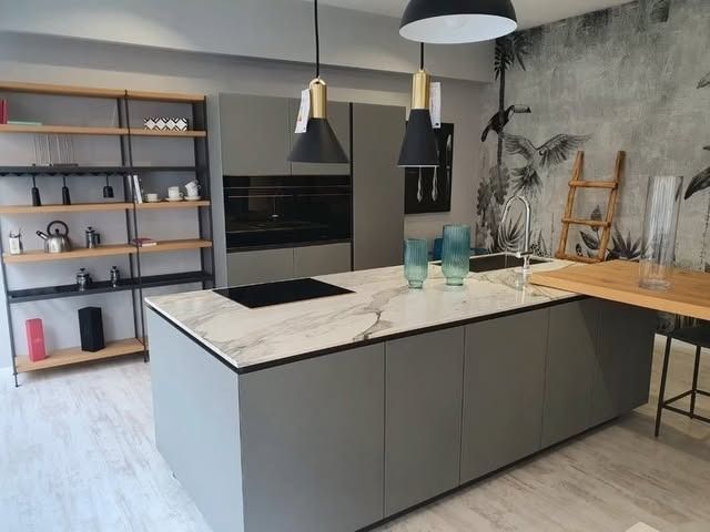 Cucina moderna con mobili grigi, isola in marmo e mensole. Lampadari neri e dorati.