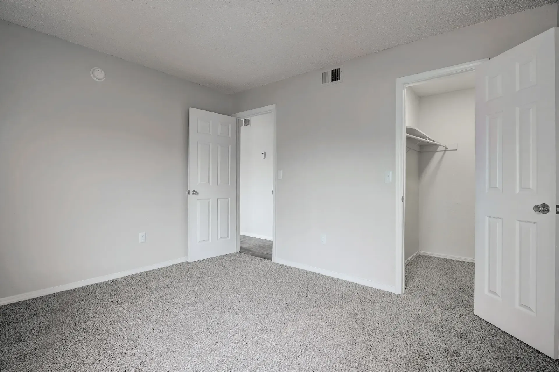 An empty living room with a carpeted floor and a ceiling fan.