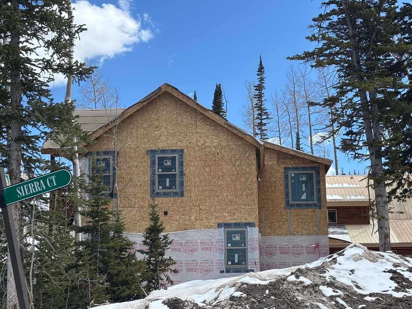 A house is being built on a snowy hill next to a street sign.