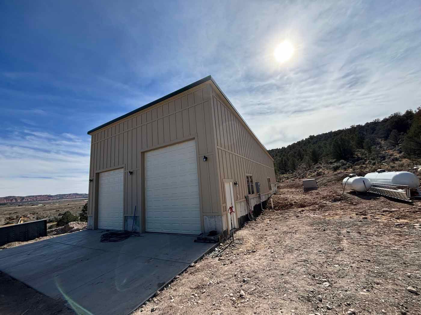 A garage with two white garage doors is sitting on top of a dirt hill.