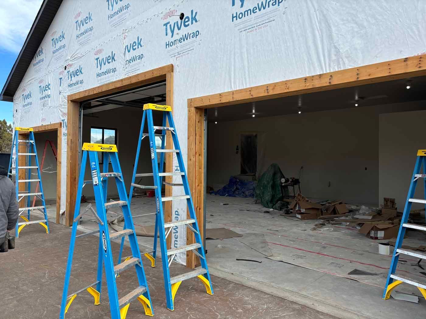 Three ladders are sitting in front of a garage under construction.
