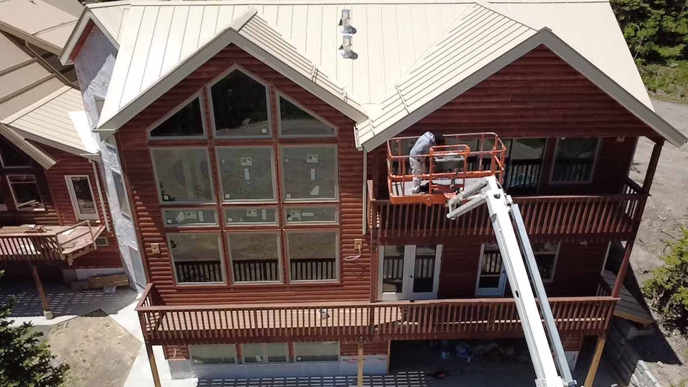An aerial view of a large log cabin being painted.