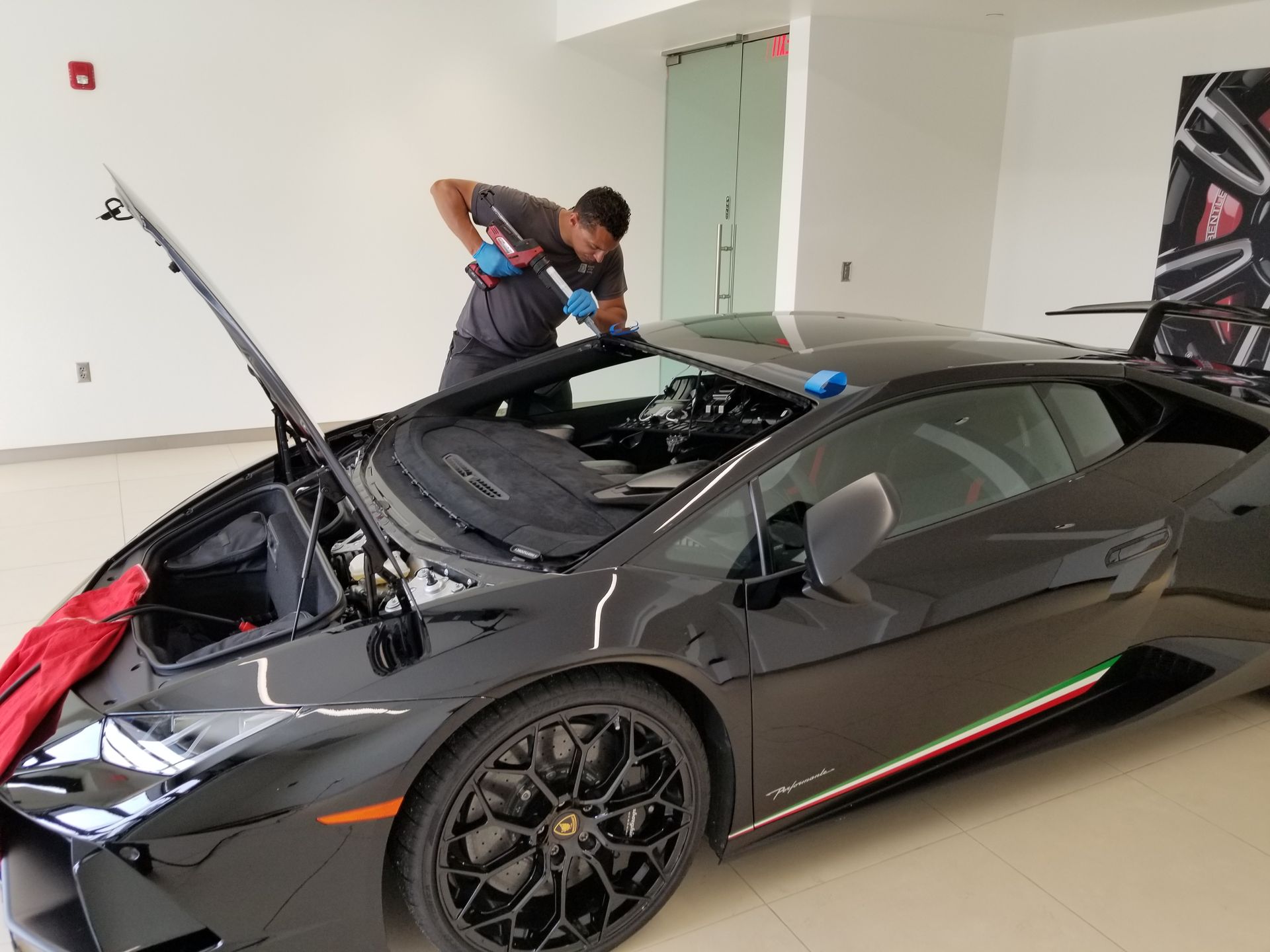 Man applying sealant to the windshield of a black Lamborghini in a garage.