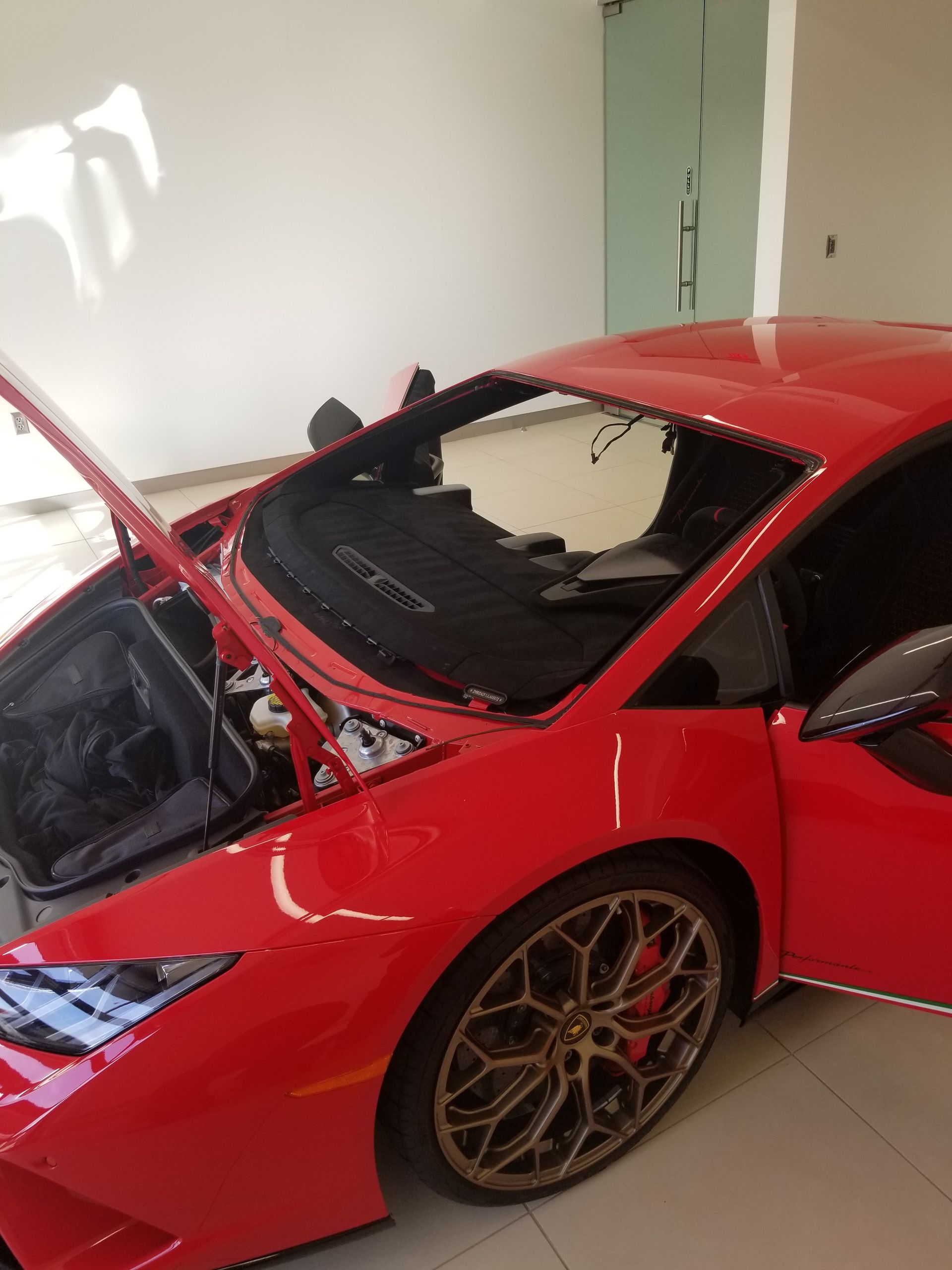 Red Lamborghini with hood and door open in a white room.