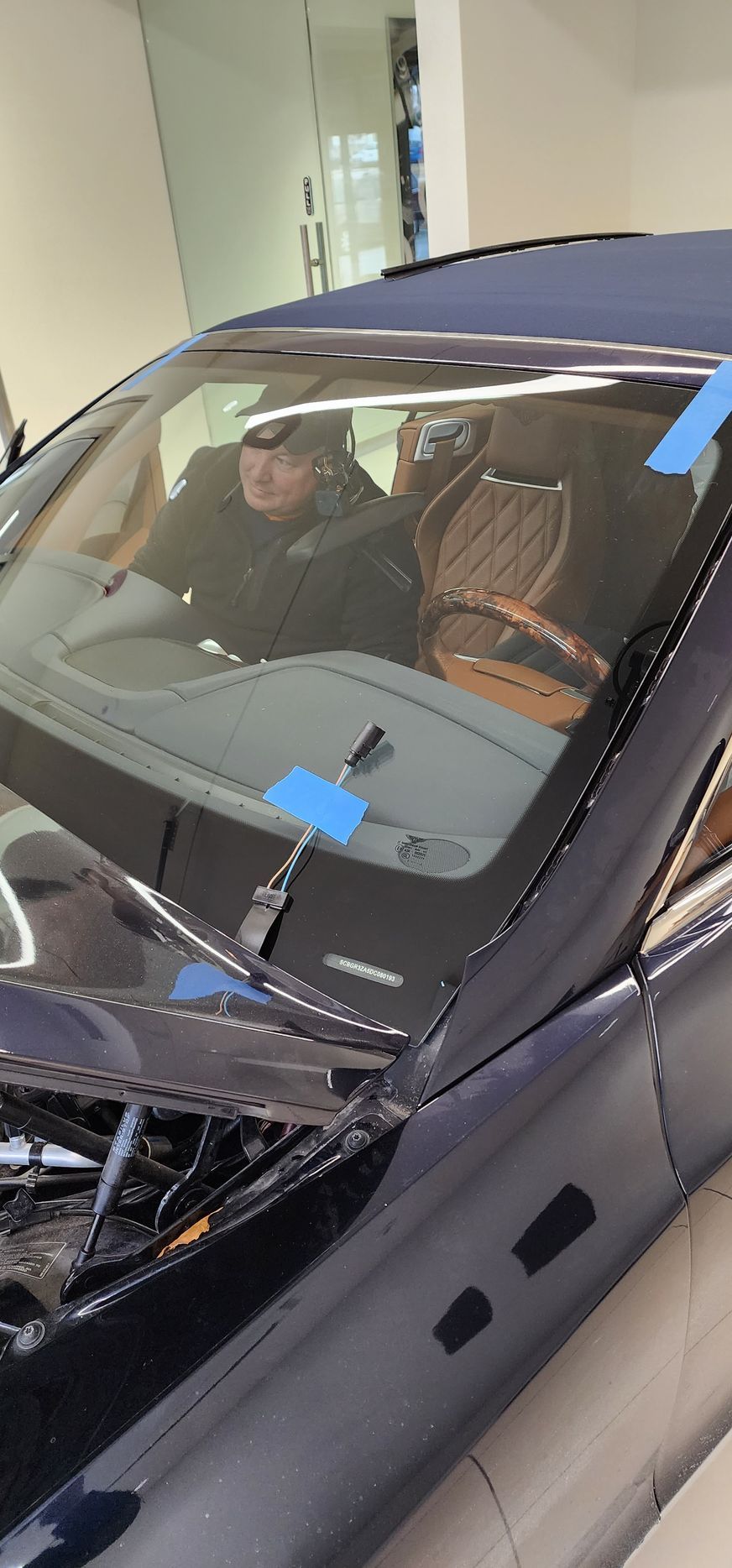 Person sitting in a navy blue convertible car with tan leather seats and a wooden steering wheel.