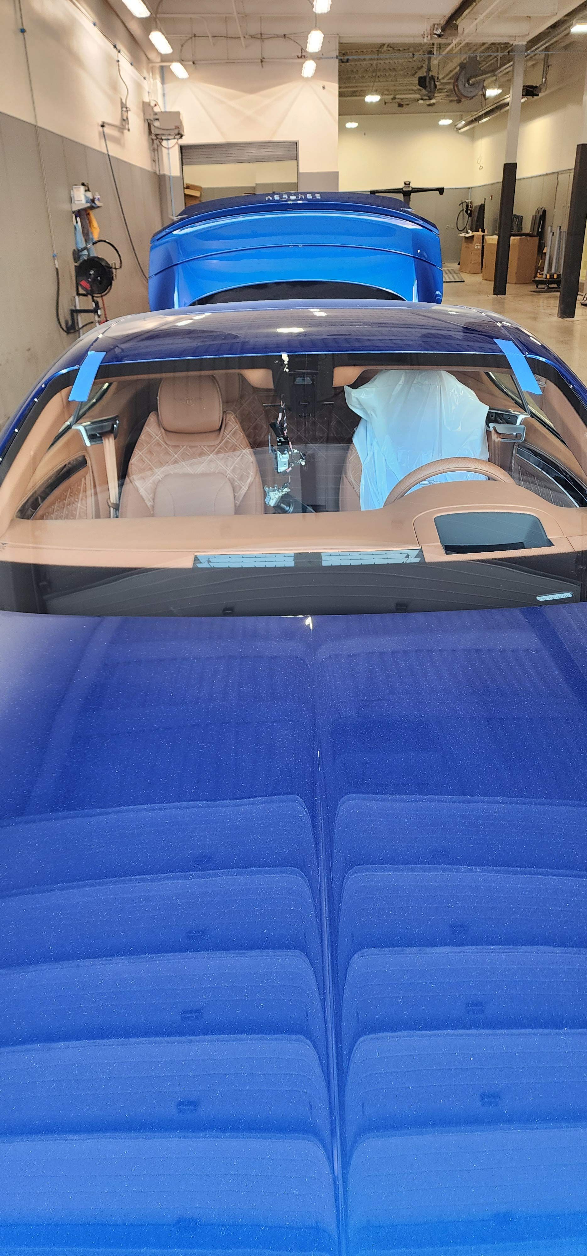 Blue sports car in a garage; interior details visible. A person is inside the car working.