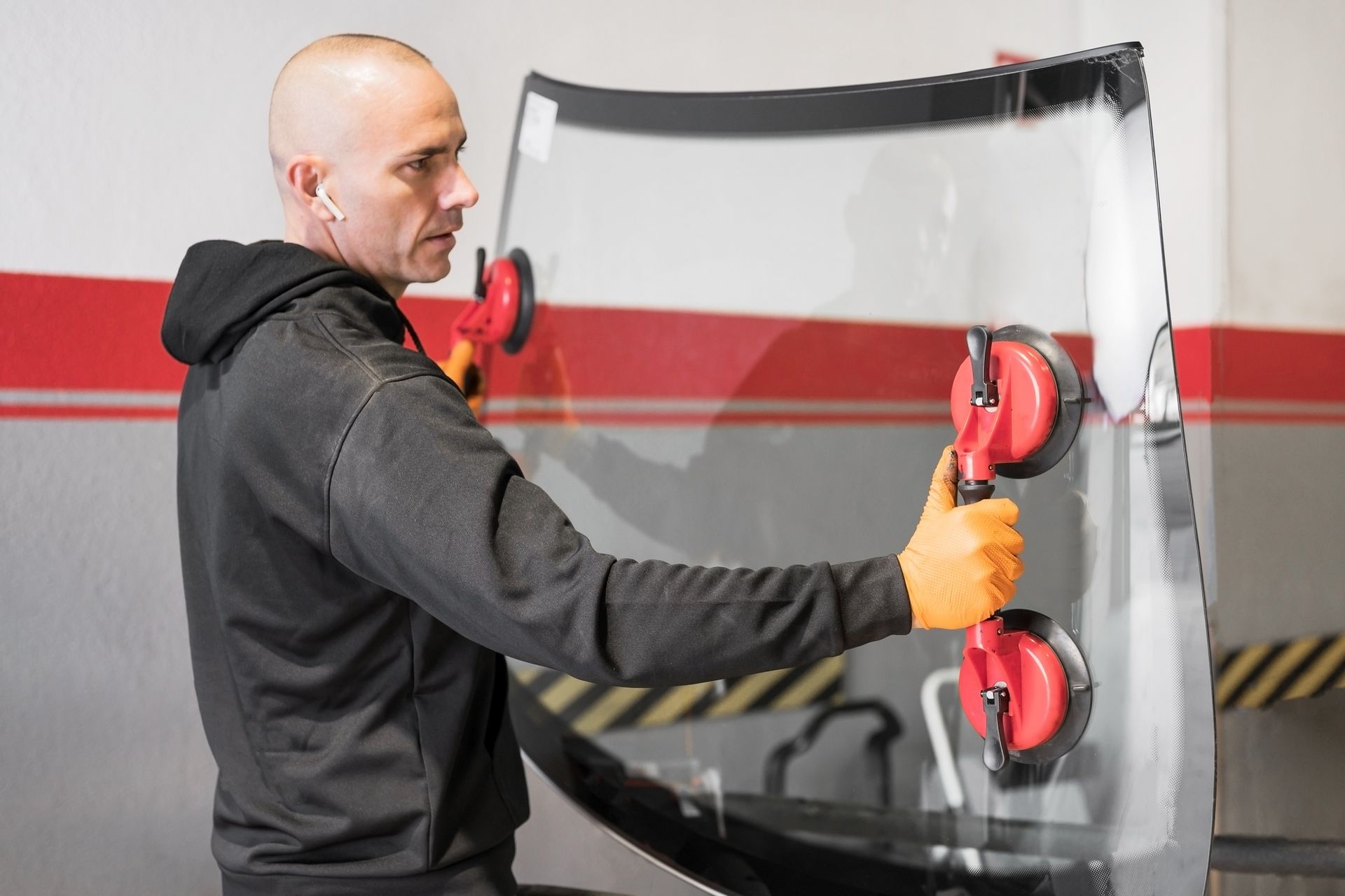 Suction-cup tools grasp windshield pane during expert windshield replacement service at auto shop. 