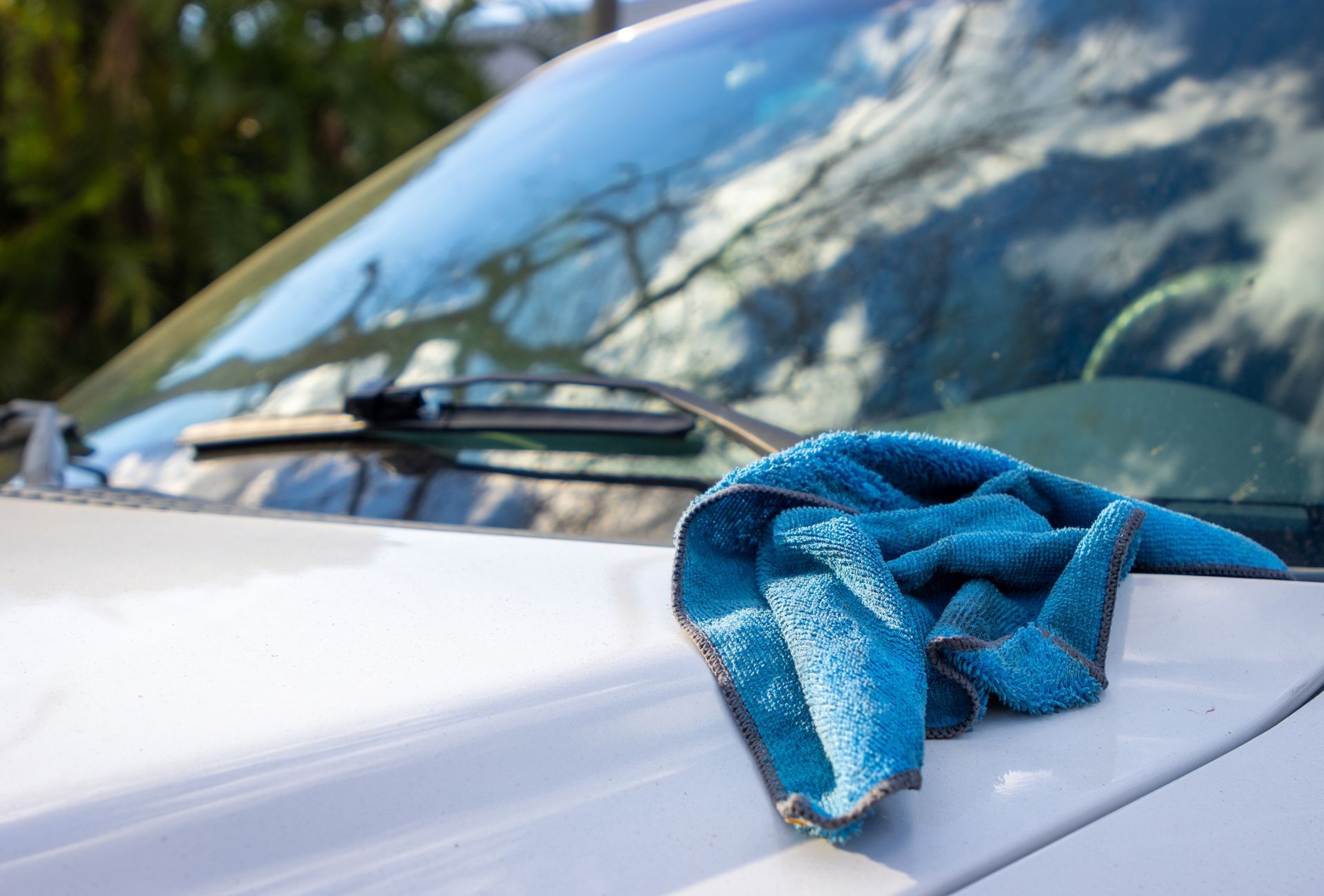 Blue microfiber cloth on the hood of a white car, windshield in the background.