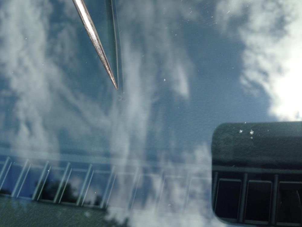 Reflections in a car windshield: sky, clouds, building with windows, and a windshield wiper.