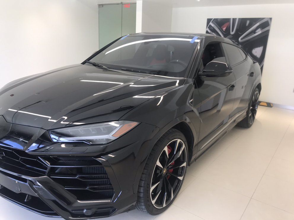 Black Lamborghini Urus SUV parked in a brightly lit showroom. Red accents on the wheels.