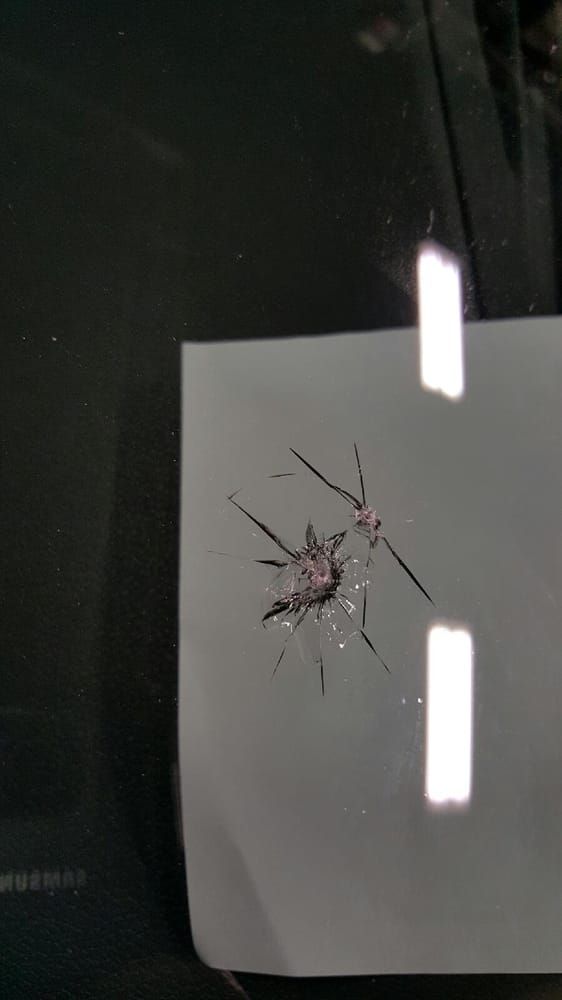 Cracked car windshield with a starburst pattern, white paper behind it, and light reflections.