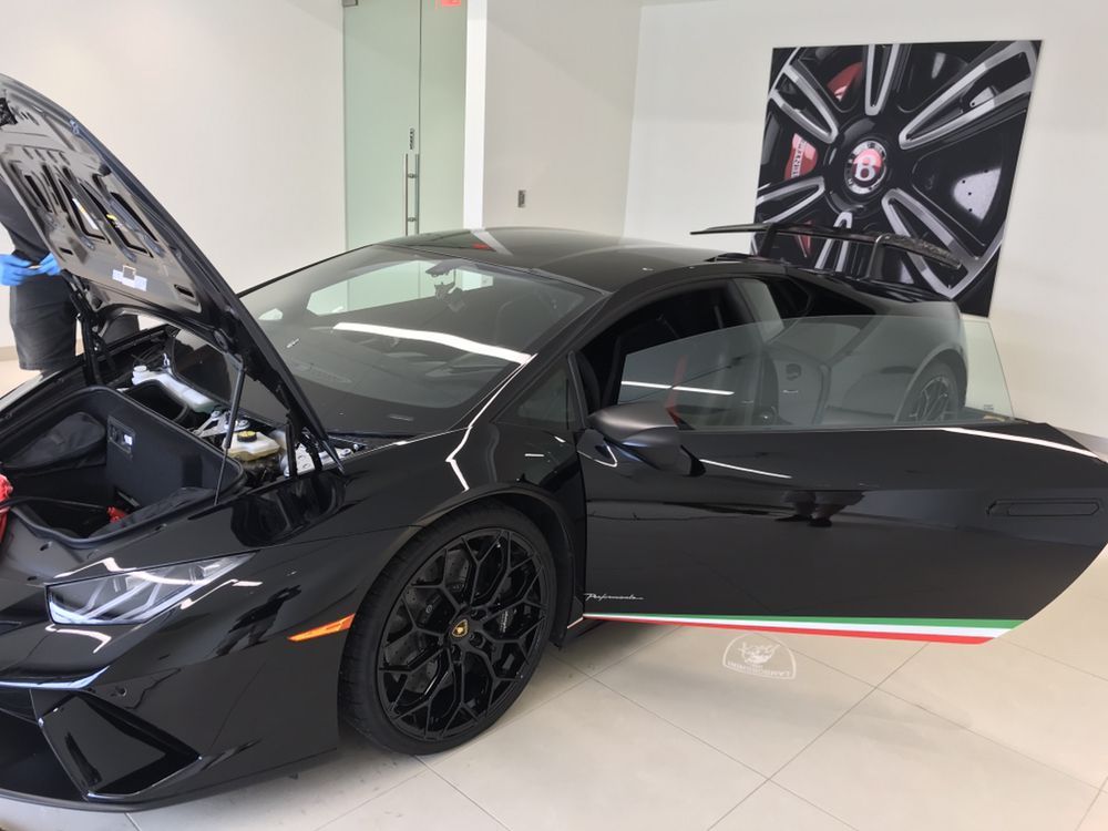 Black Lamborghini with open hood and door, parked indoors with Italian flag stripe detail.