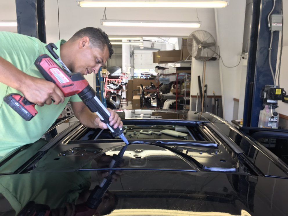 Man in green shirt applies sealant to a car roof in a repair shop.