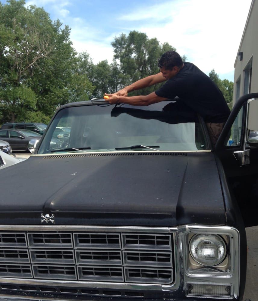 Man on a black truck applying tint film to windshield. Sunny day.