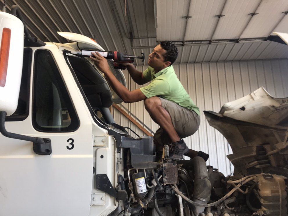 Man applying sealant to a truck windshield in a garage.