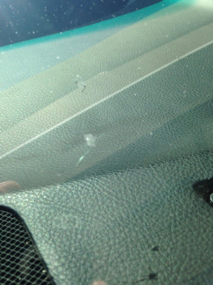 Windshield with a small chip in the glass, viewed from inside a car, dashboard visible.