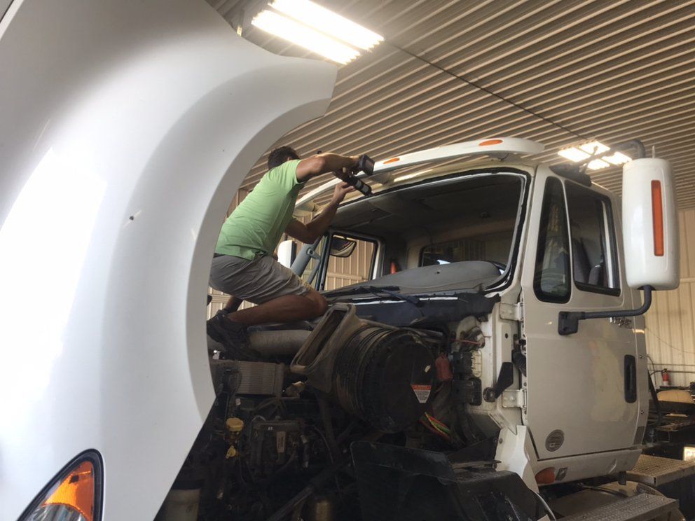 Person replacing windshield on white semi-truck in a garage.