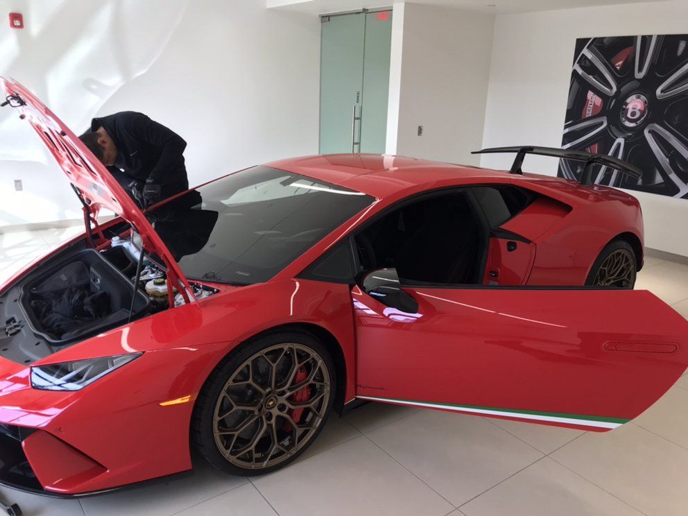 Red Lamborghini with open hood and door, mechanic working inside. Interior shot.
