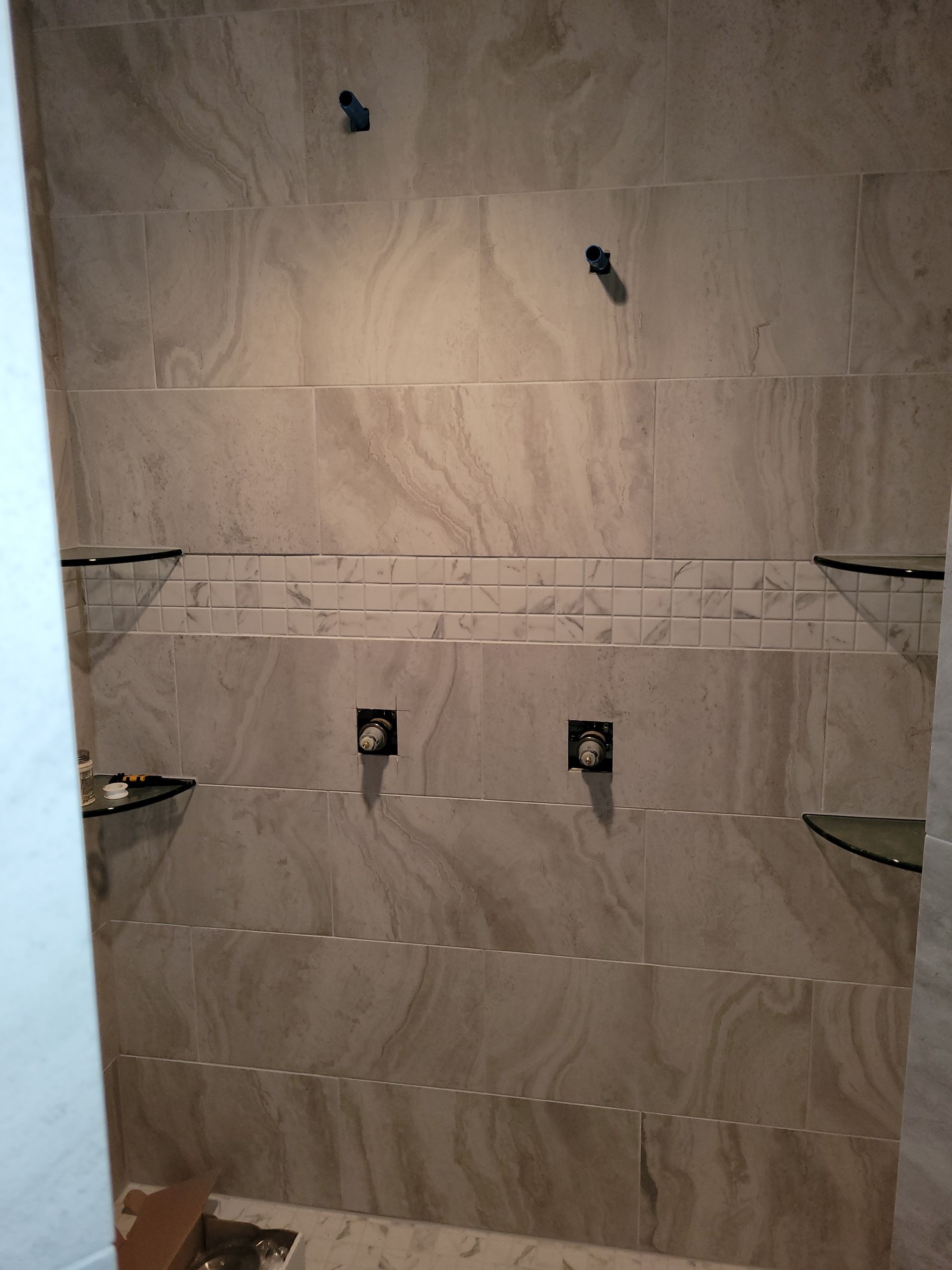 A bathroom with a tiled wall and a glass shelf.