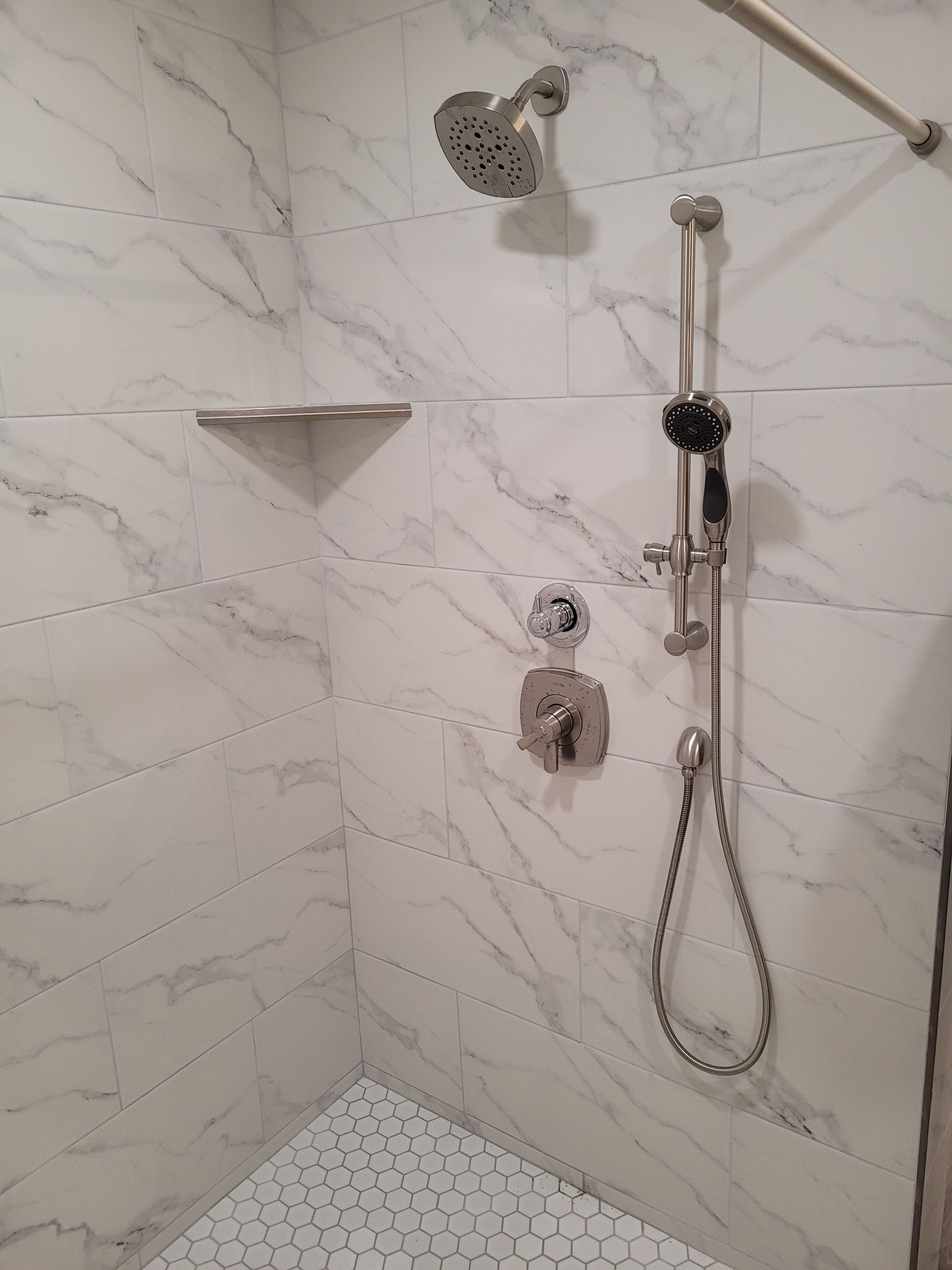 A shower with a shower head and a shelf on the wall.