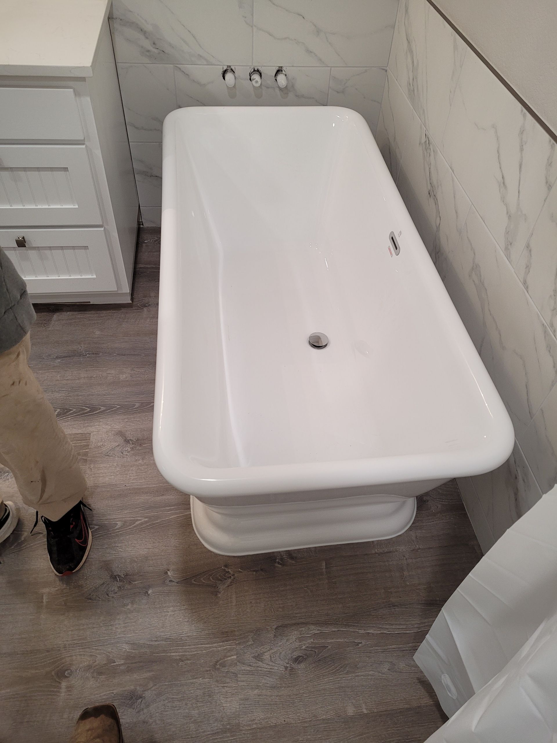 A person is standing next to a white bathtub in a bathroom.