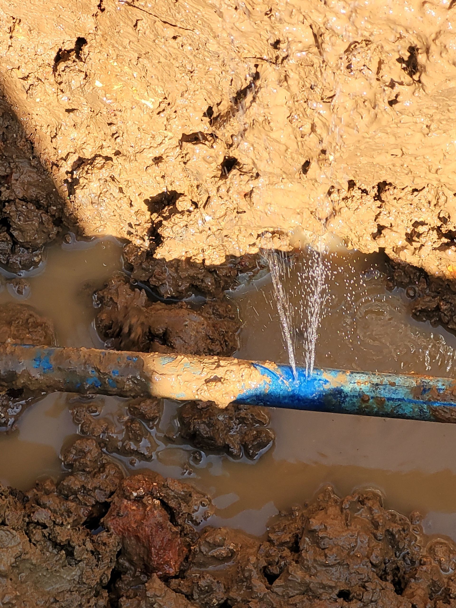 A blue pipe is leaking water in the mud.