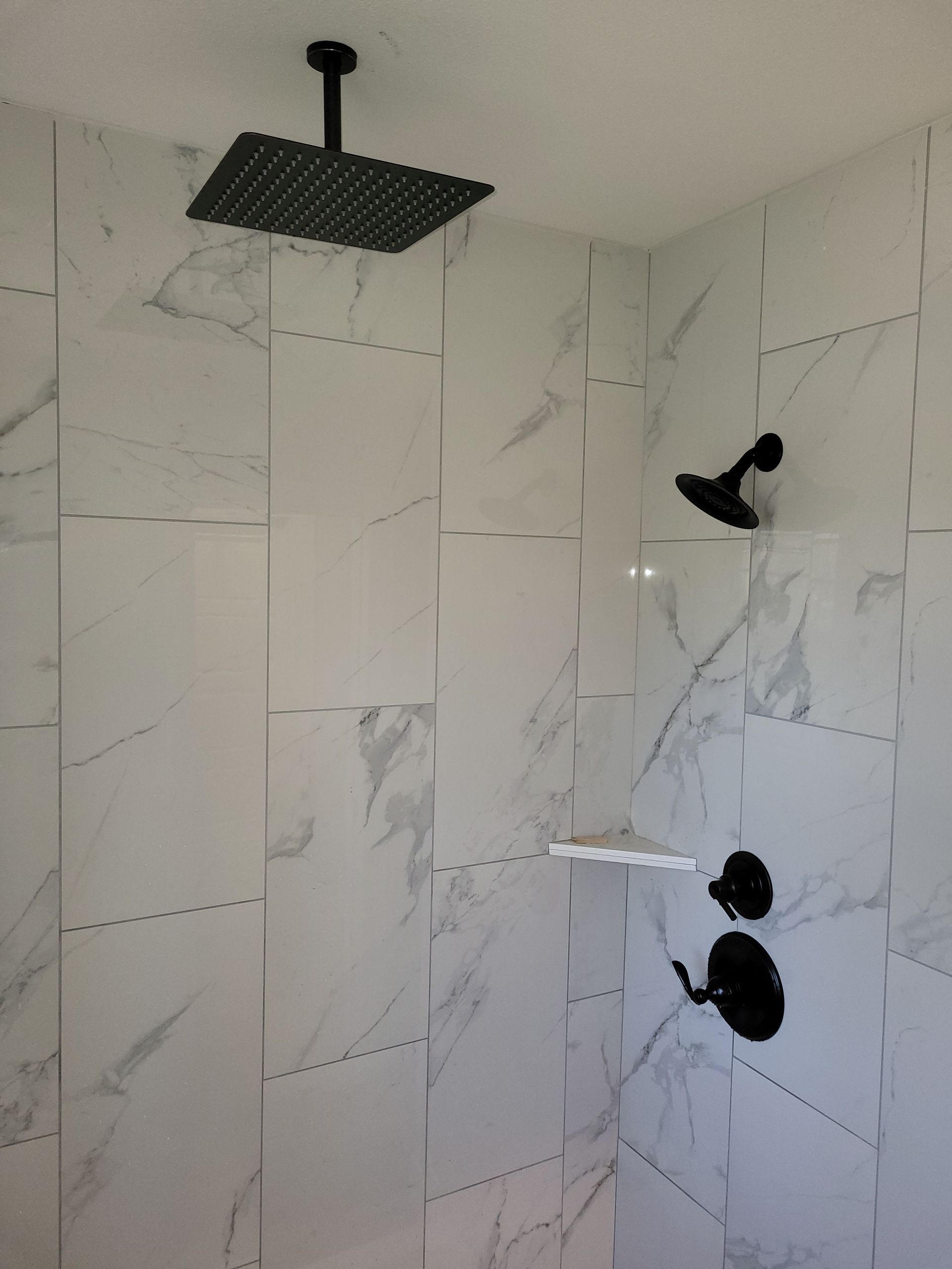 A shower with white tiles and a black shower head