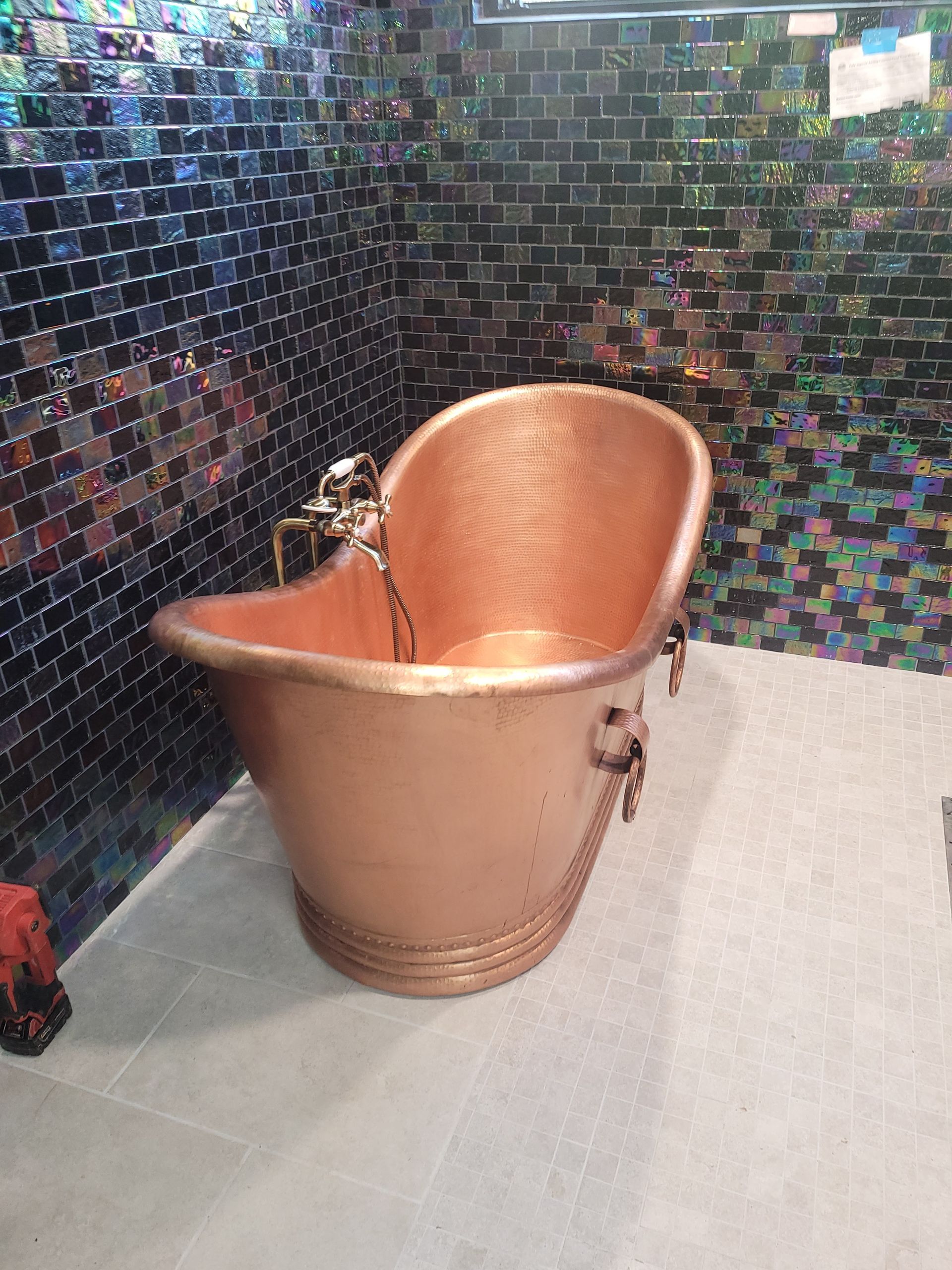 A copper bathtub is sitting in a bathroom next to a brick wall.