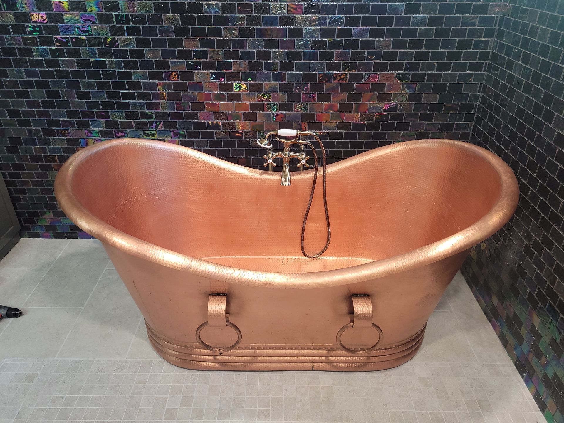A copper bathtub is sitting in a bathroom next to a brick wall.