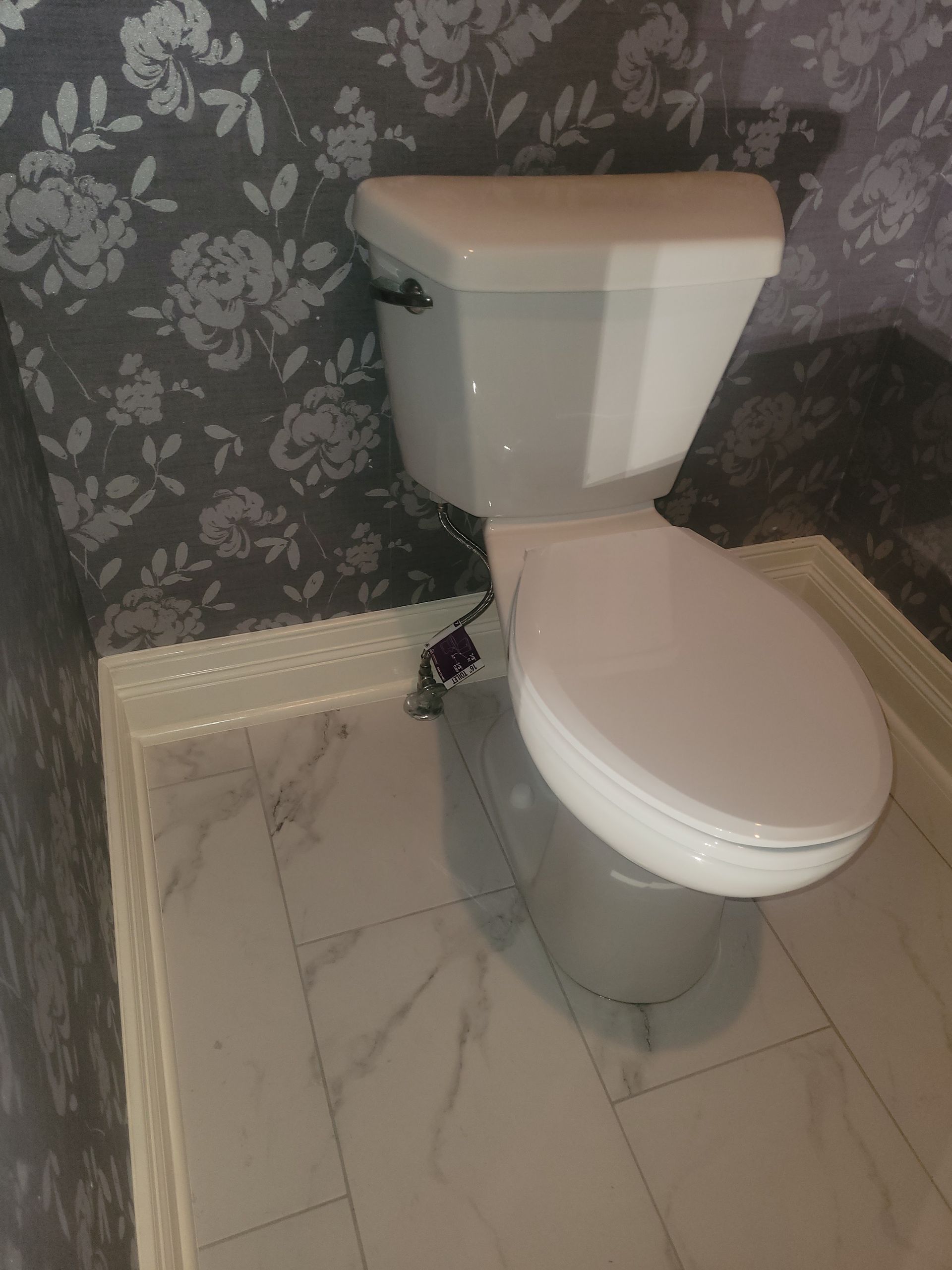 A white toilet is sitting on a tiled floor in a bathroom.