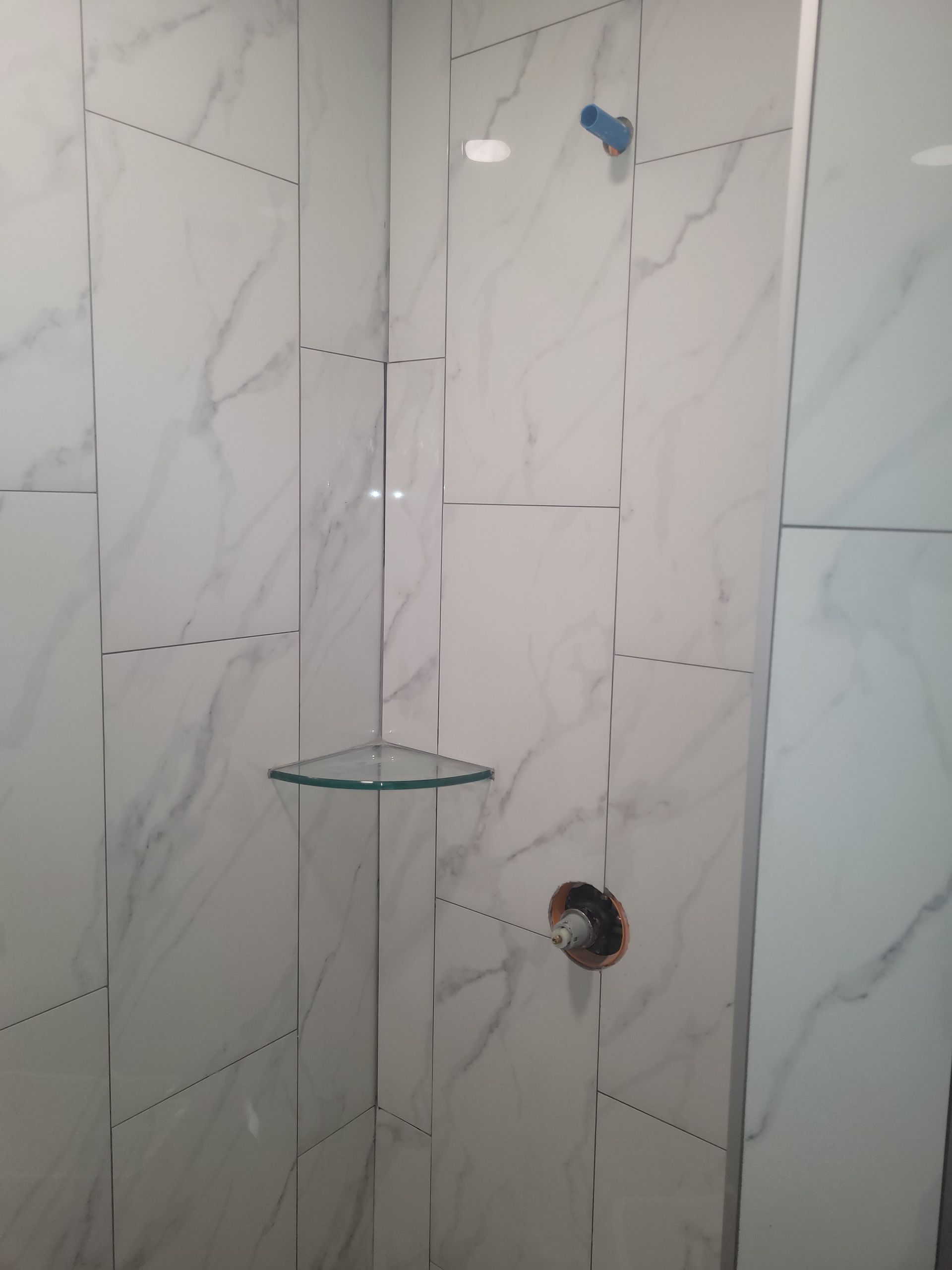 A bathroom with white tiles and a glass shelf
