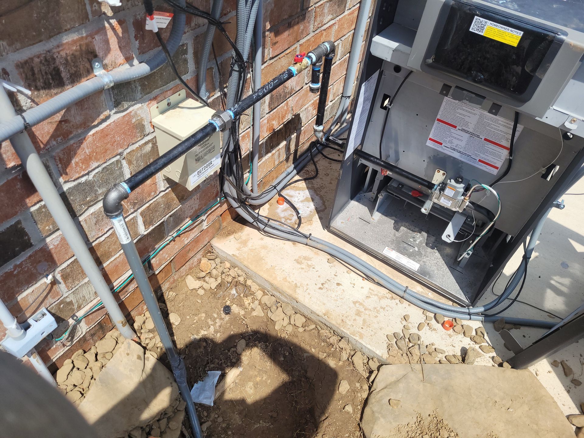 An air conditioner is sitting in the dirt next to a brick wall.