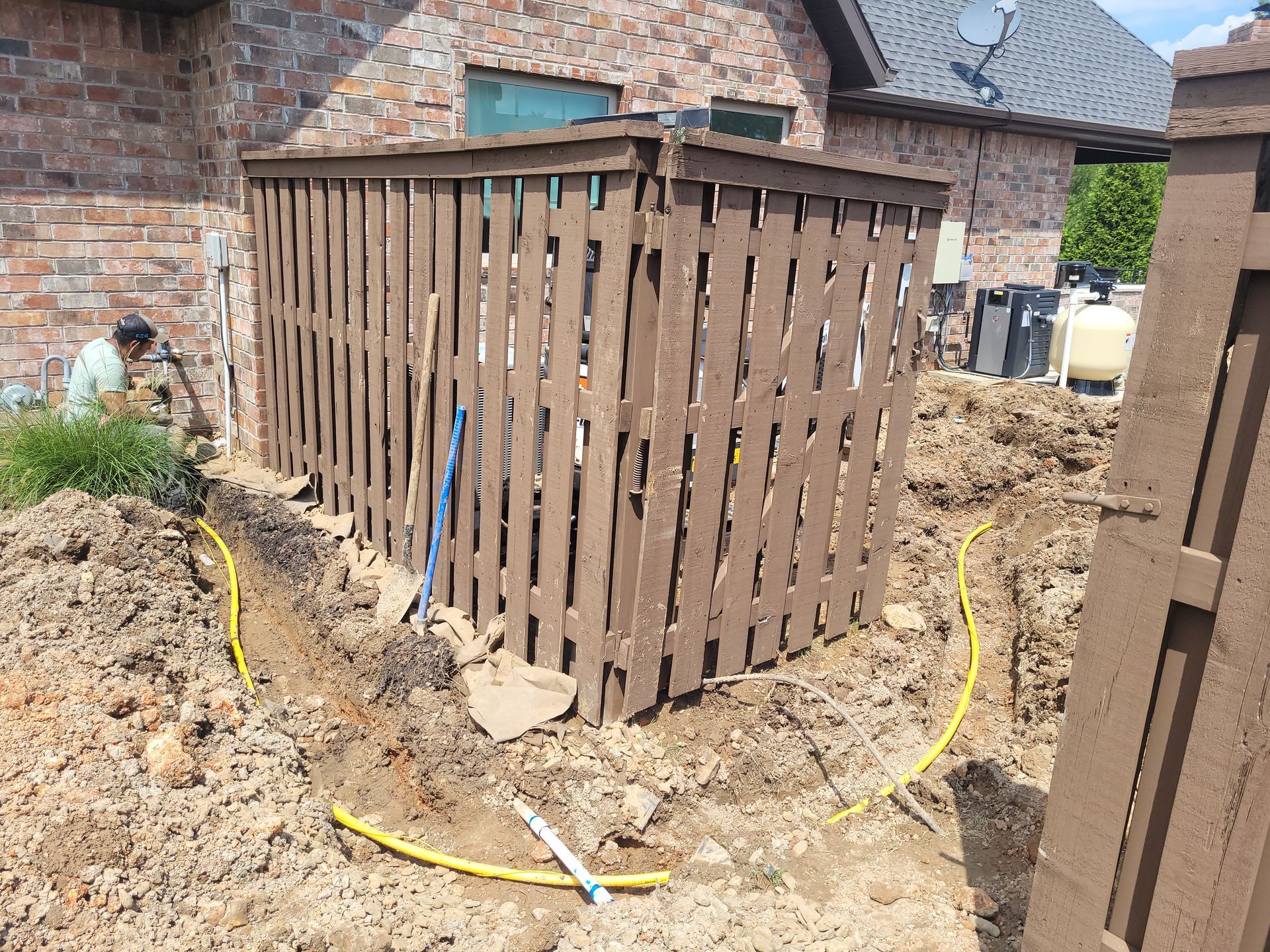 A wooden fence is being built in the dirt in front of a brick house.