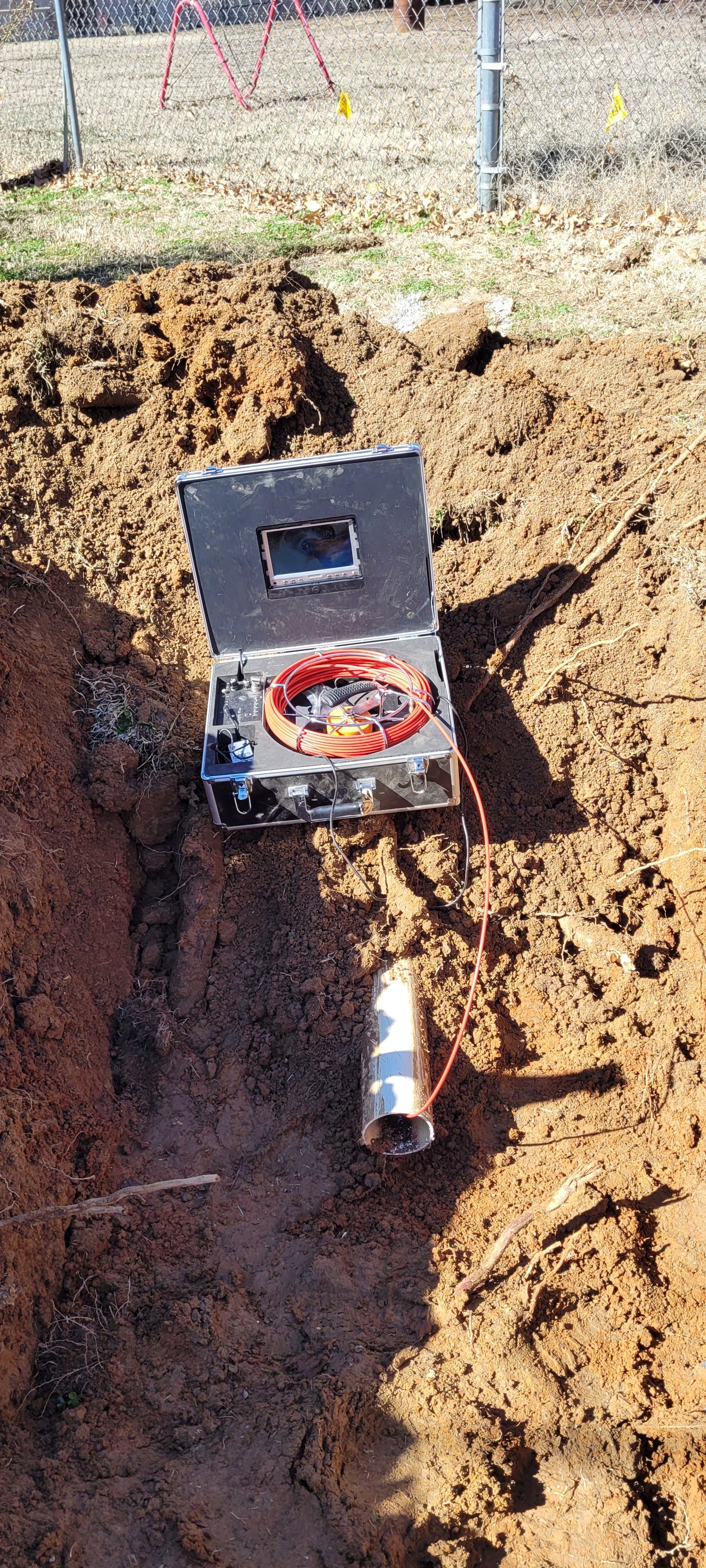 A camera is sitting in the dirt next to a pipe.