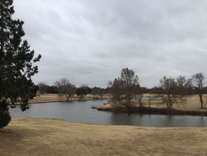 Meadowlake park, a popular spot in Enid, OK, with a pond that curves around banks of brown grass spotted sparsely with trees.