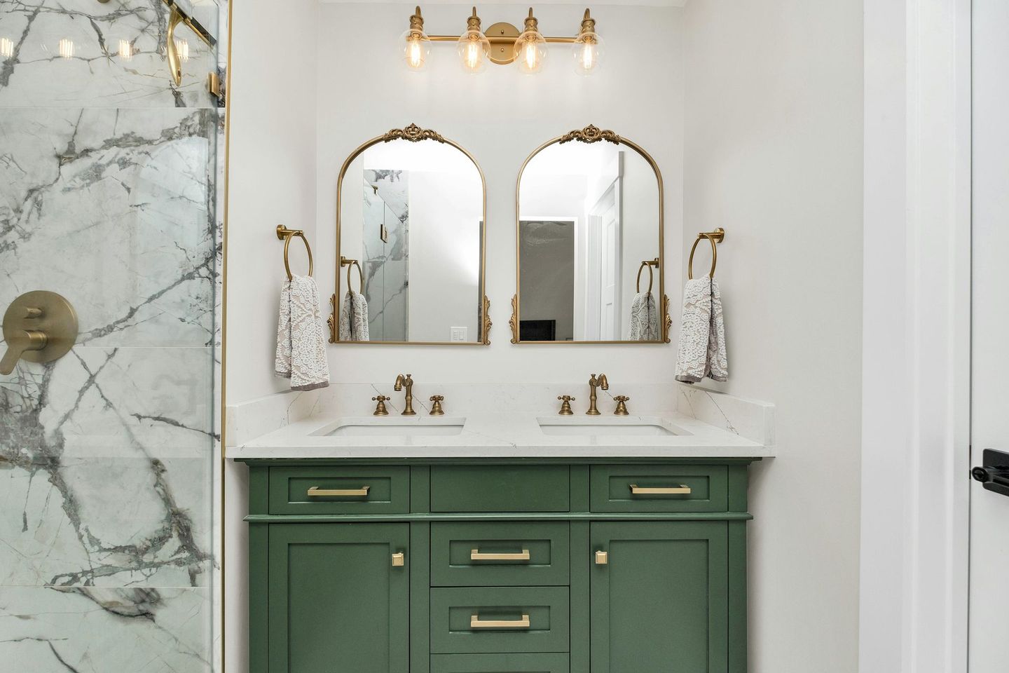 A bright green double vanity with classy brass fixtures antique looking mirrors and a grey-veined marble shower.