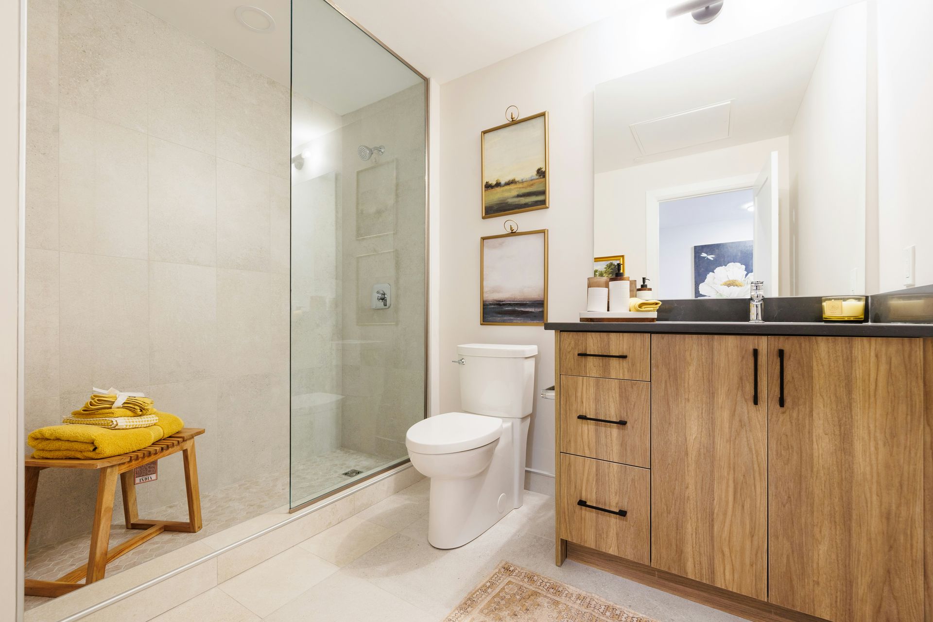 A traditional barrier-free shower with a single panel of glass and neutral beige stone is next to a toilet and single vanity.