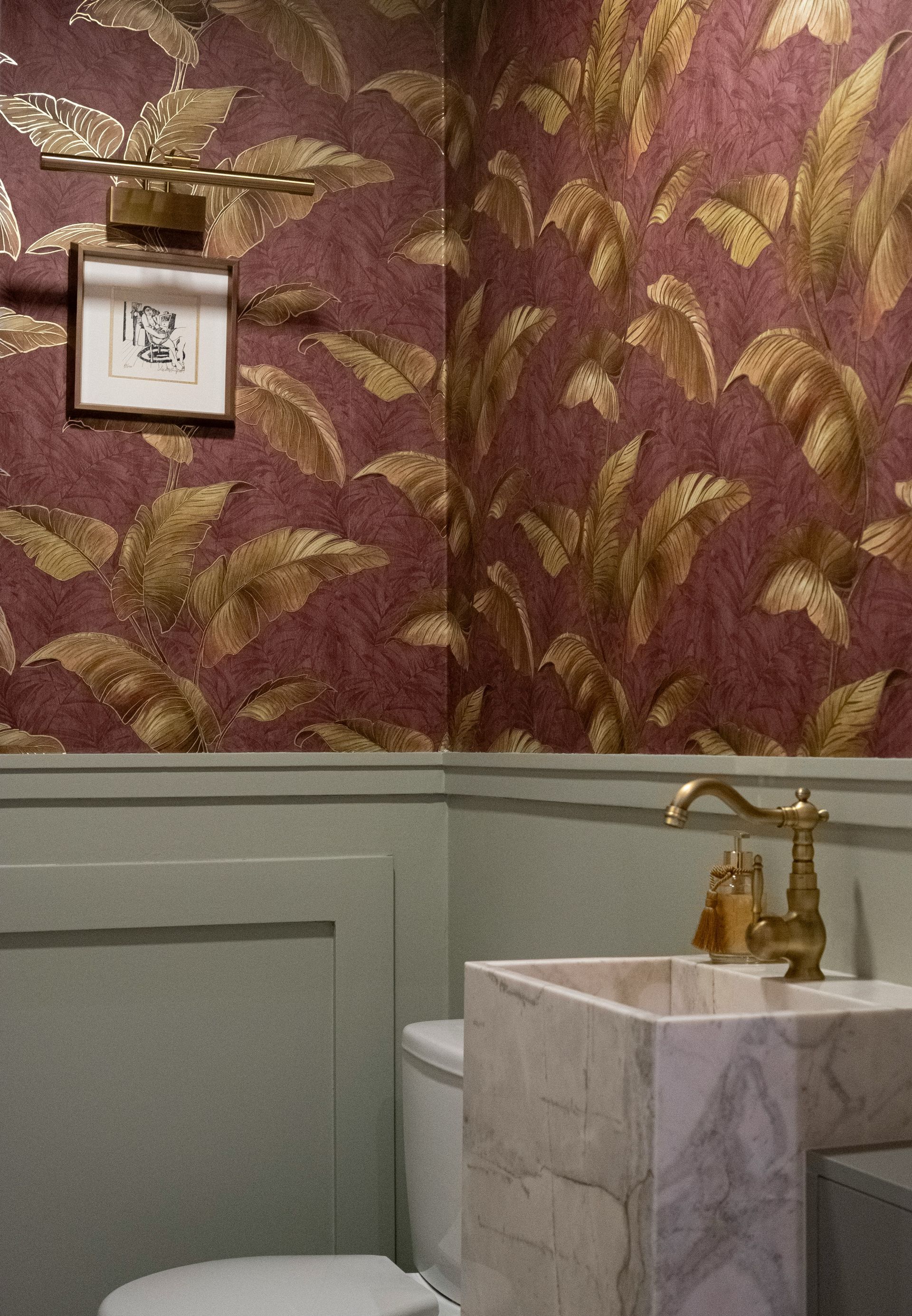 A marble-basined sink with antique brass fixtures surrounded by a richly printed gold and rust wallpaper.