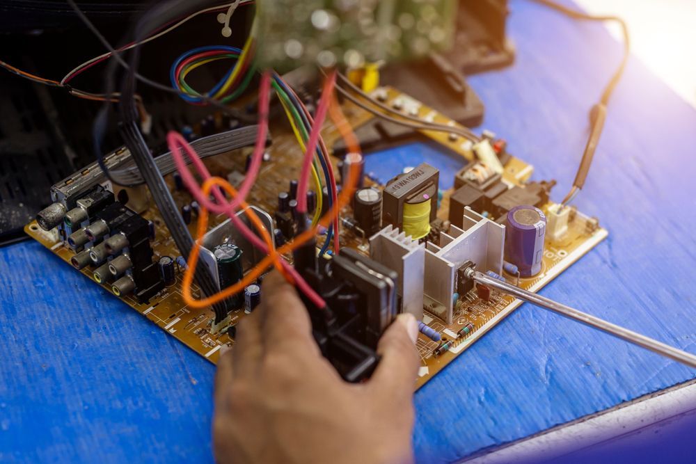 Person's Hand Working on a Circuit Board With Wires and Components on a Blue Surface — Pete's Auto Electrical in Cranbourne, VIC