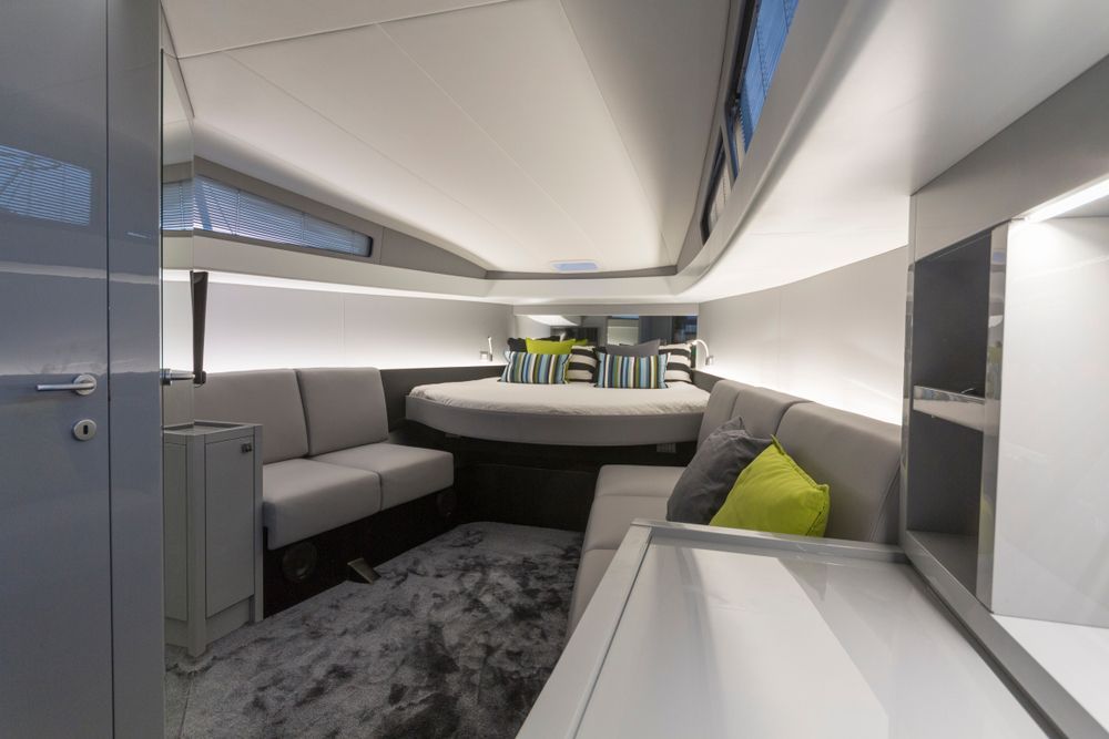 Interior of a modern boat cabin with a sofa, bed, and built-in storage. Gray, white, and green color scheme. — Pete's Auto Electrical in Cranbourne, VIC