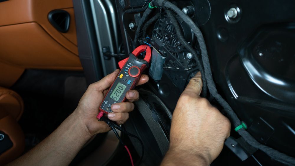 Person using a clamp meter to test wires inside a car door. The meter shows a reading. — Pete's Auto Electrical in Cranbourne, VIC