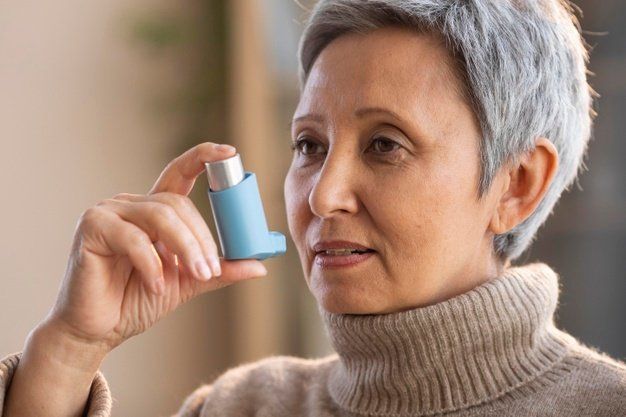 middle aged woman in turtleneck sweater holding an inhaler to her mouth
