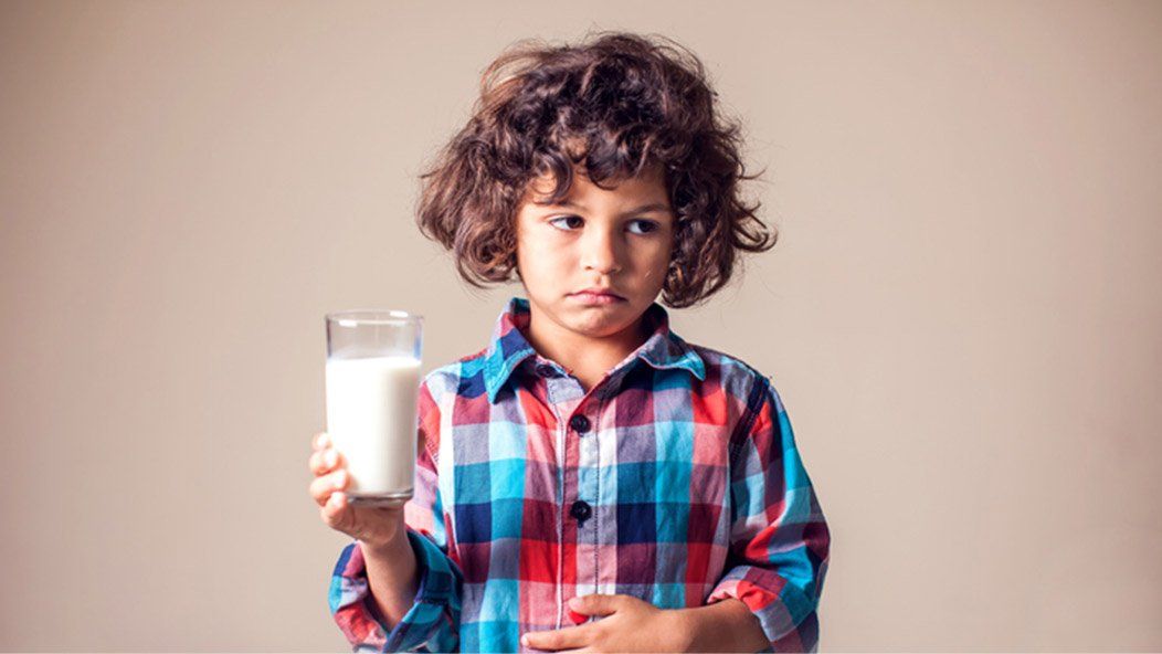 Young boy who is allergic to dairy holds a glass of milk while holding his stomach