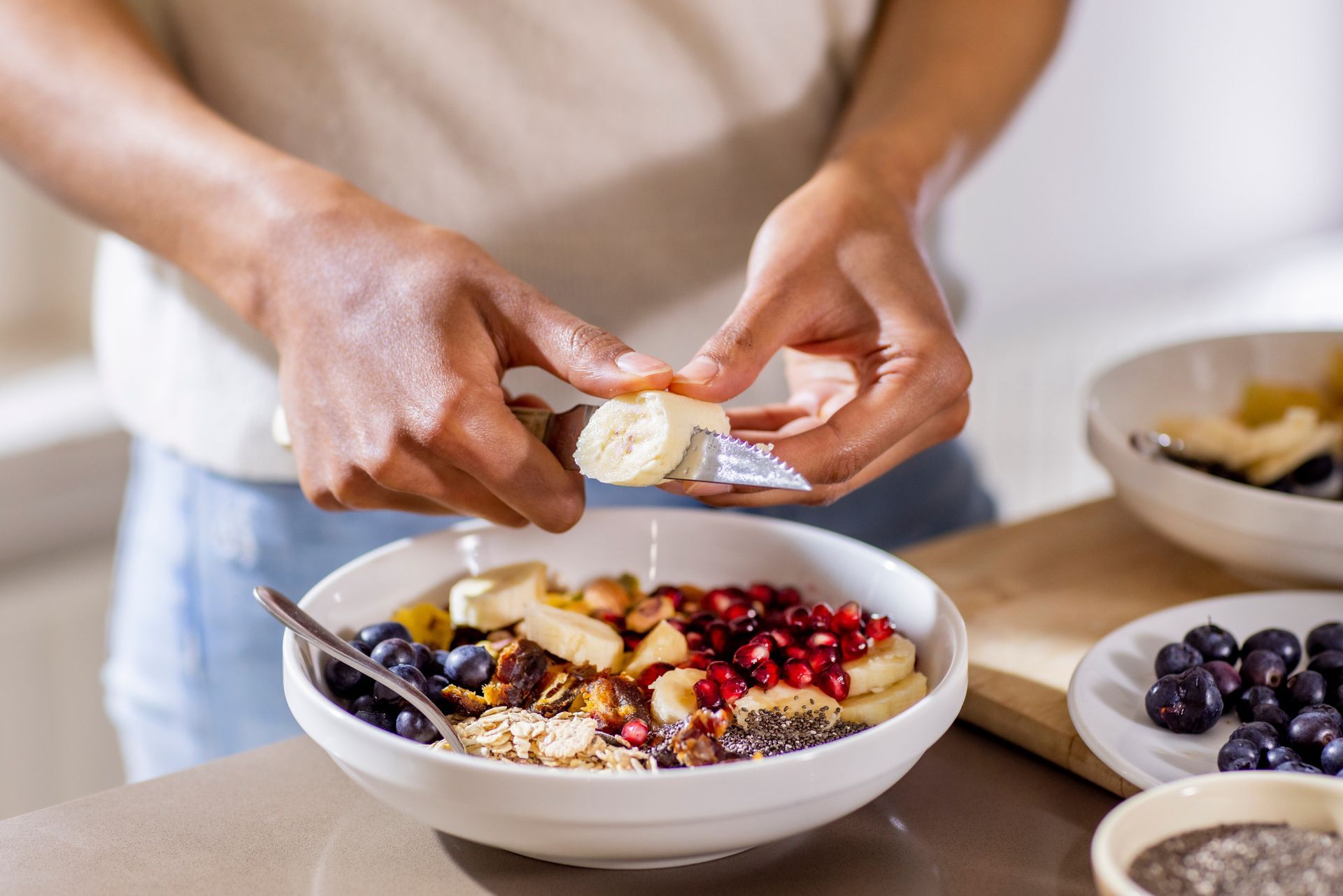 A person is putting a banana in a bowl of cereal.